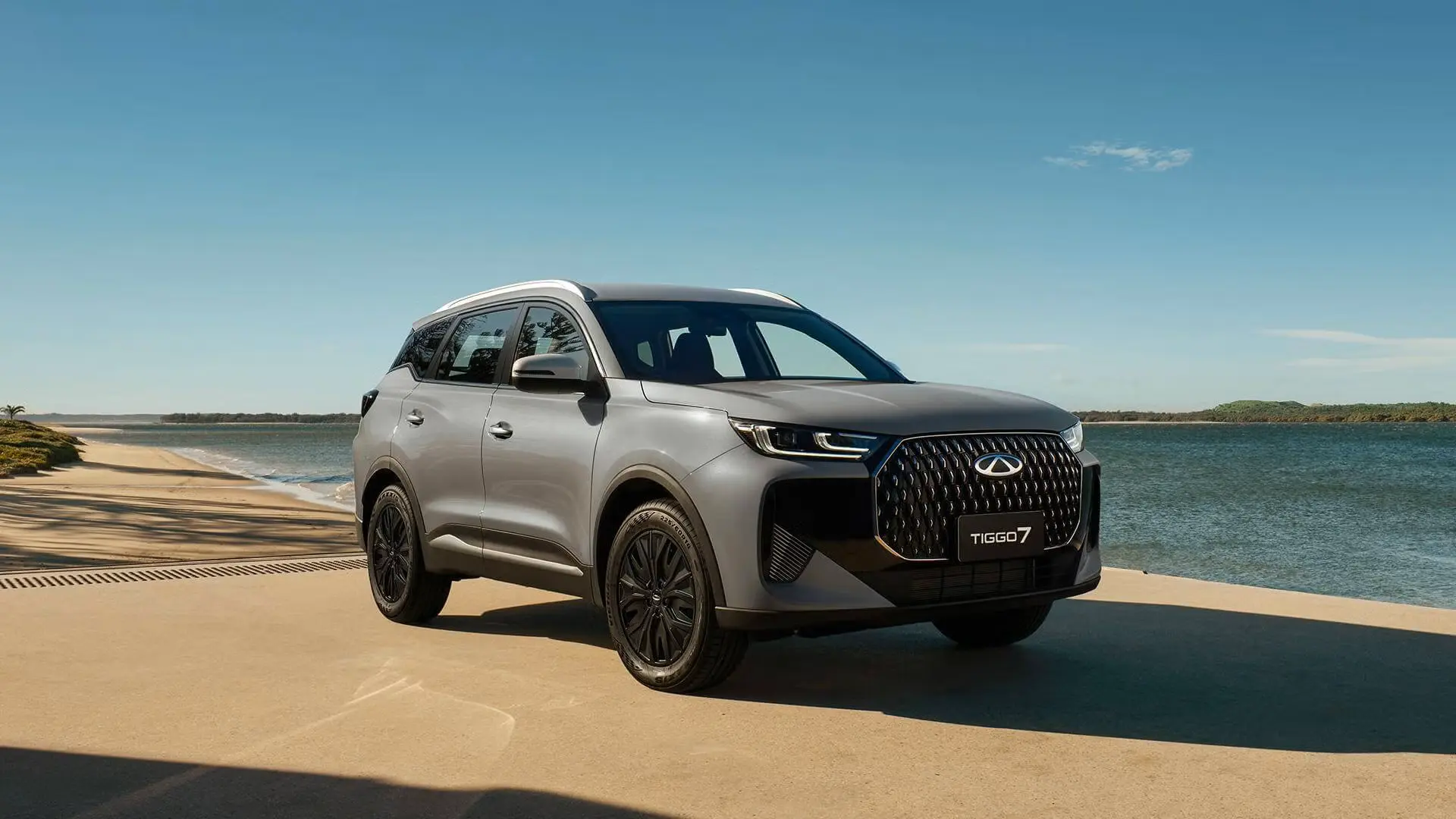 Silver MY26 Chery Tiggo 7 PHEV SUV parked by the coast, featuring a diamond grille, LED matrix headlights, and black alloy wheels, available at Chery Midrand.